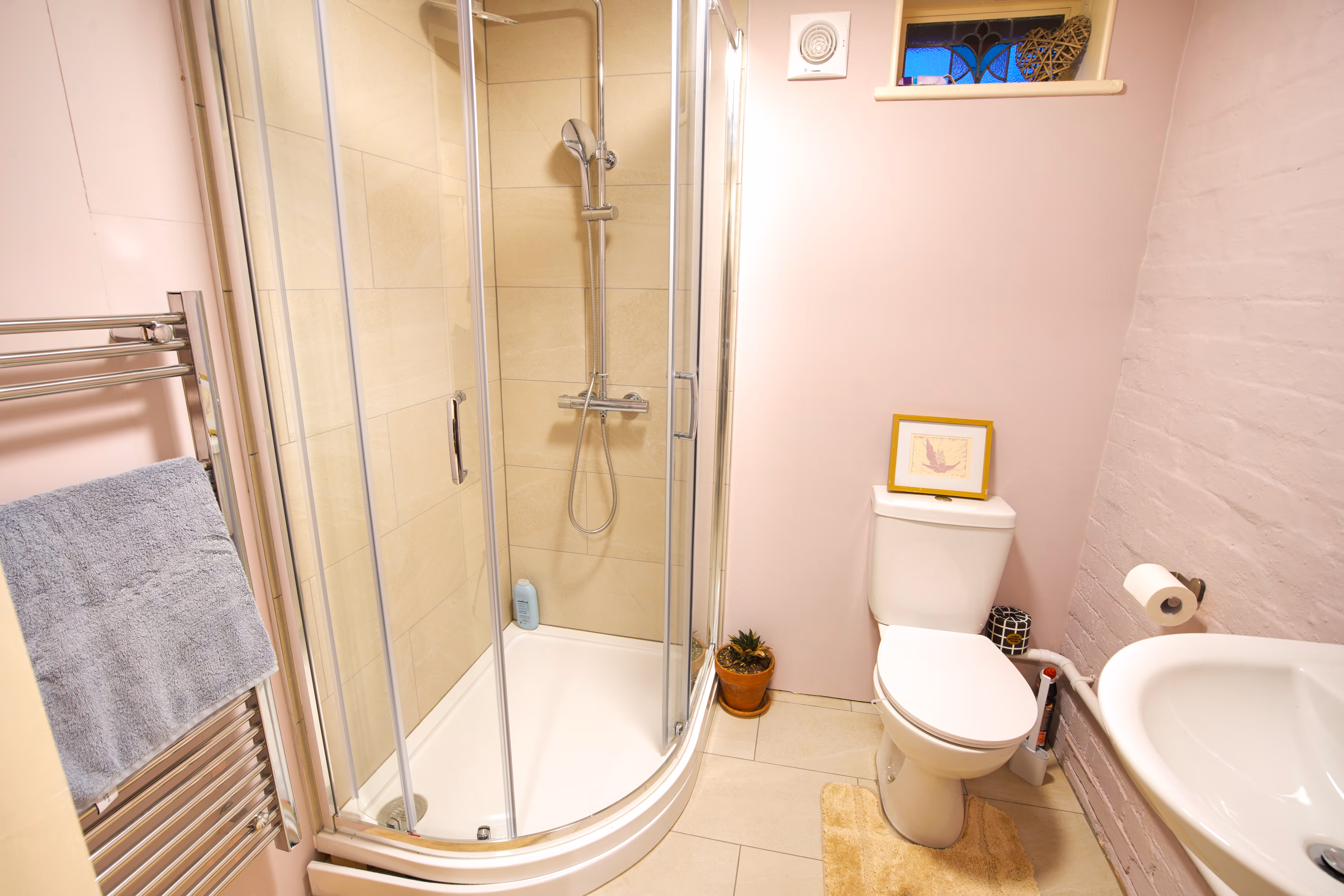 The bathroom — shower, toilet, sink, soft pink walls.